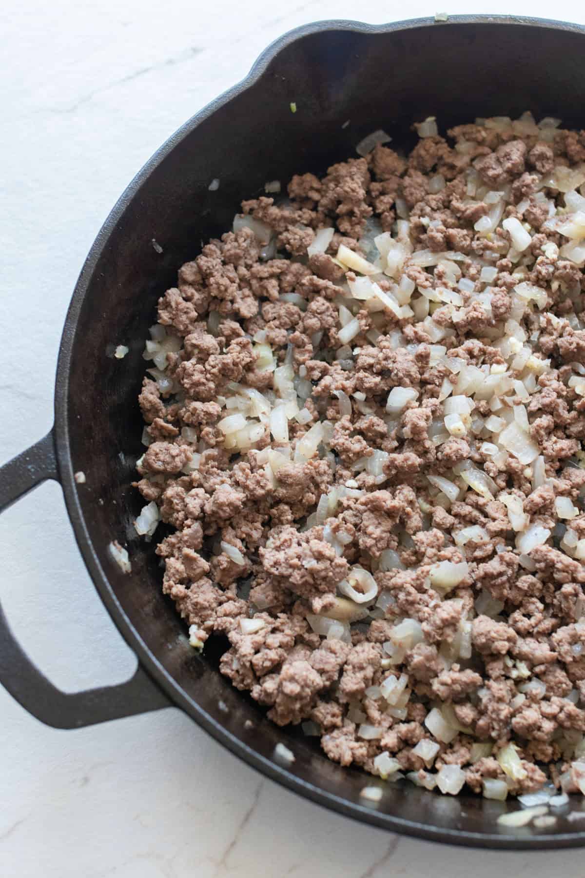 Ground beef and chopped onion in a cast iron skillet.