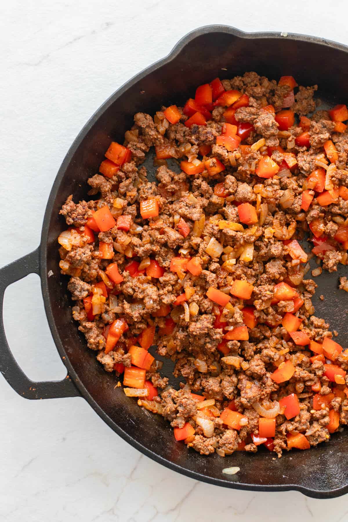 Spices and chopped peppers added to cooked ground beef in a cast iron skillet.