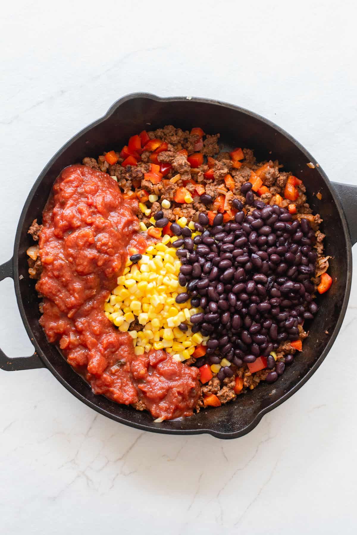 Corn and black beans added to a cast iron skillet with ground beef.