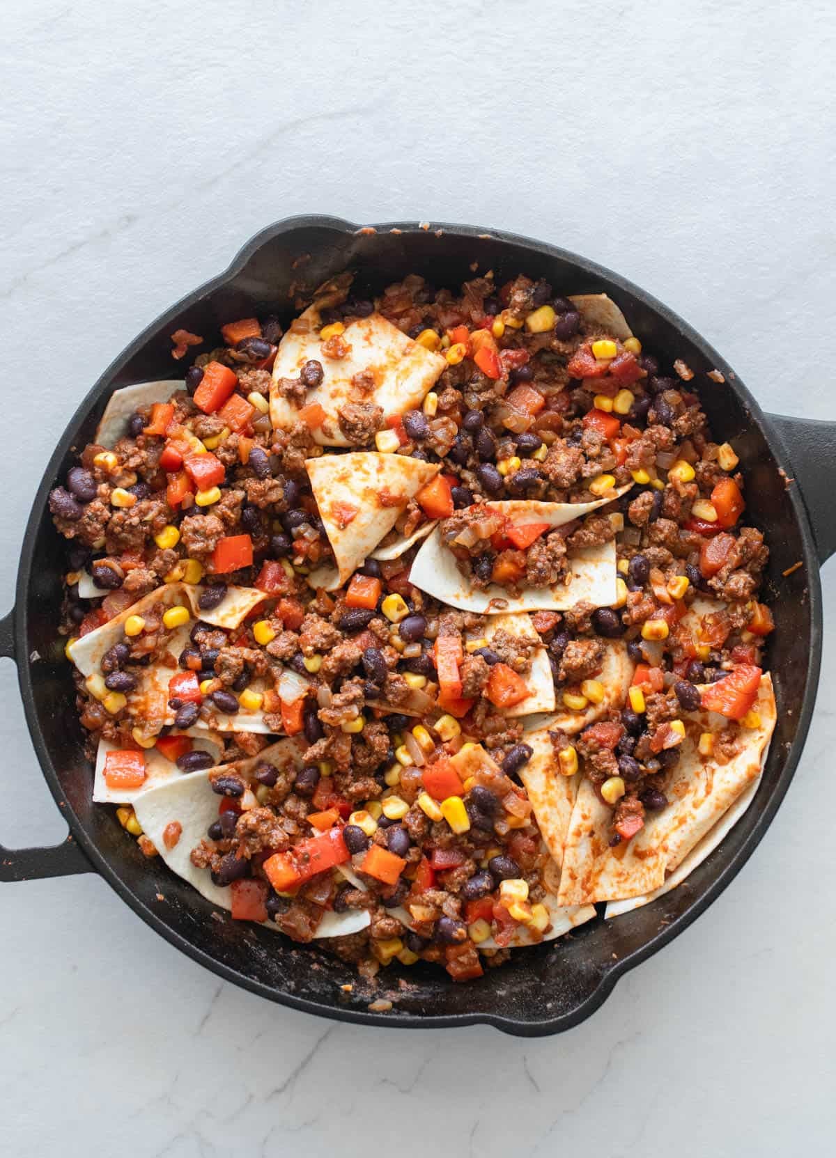 Tortilla pieces placed in ground beef mixture in cast iron skillet.