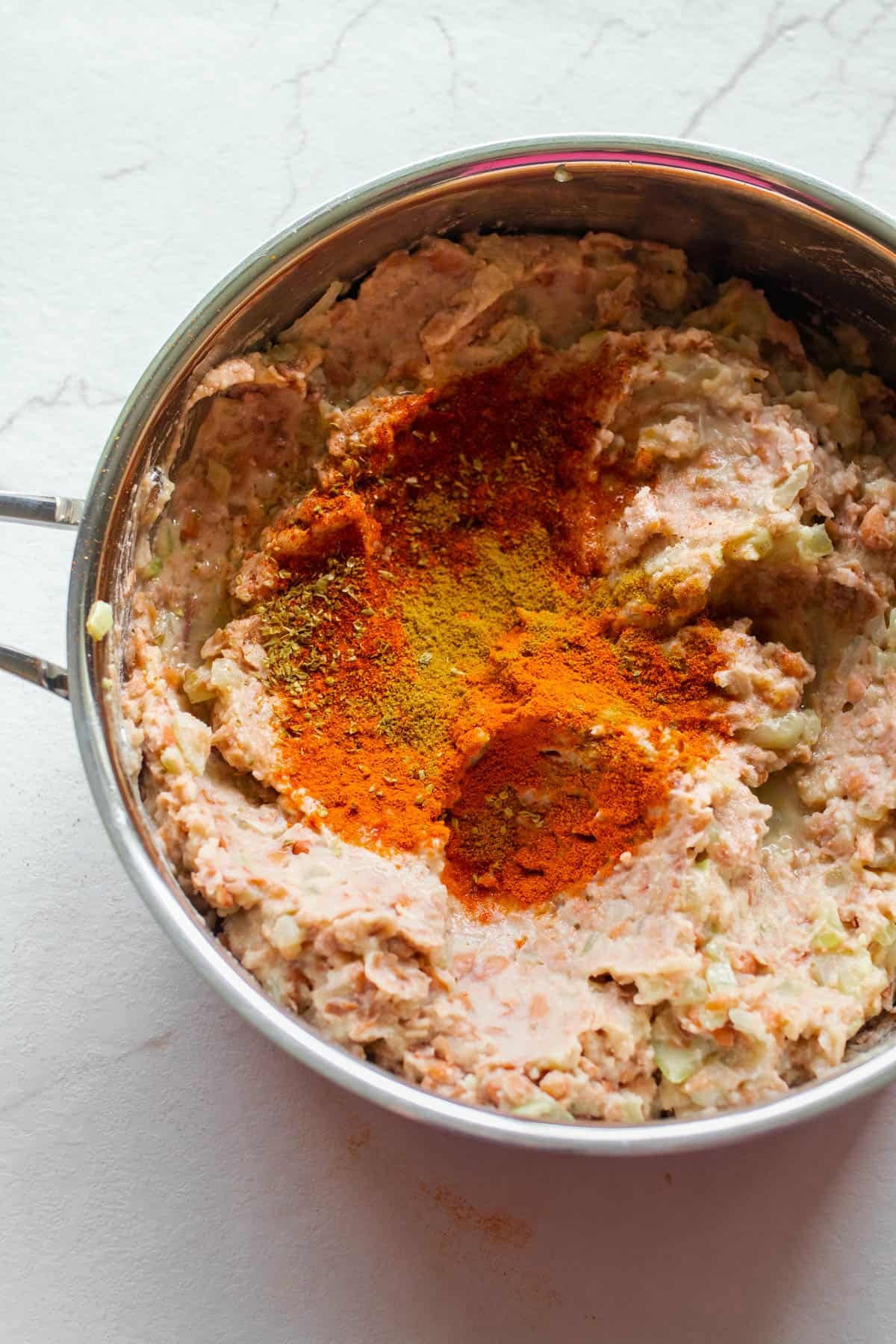 Mashed pinto beans with spices in a sauce pan.