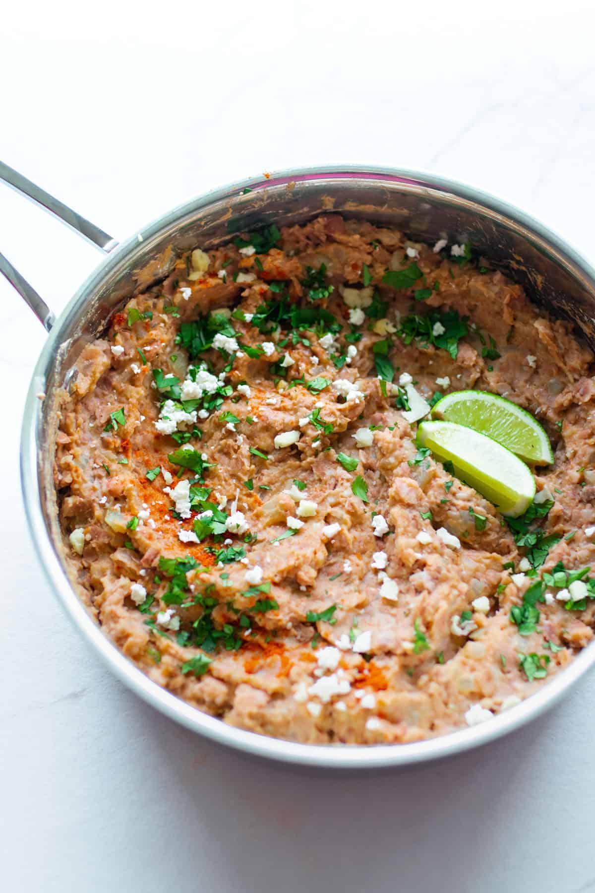 A sauce pan of homemade refried beans with garnishing on top.