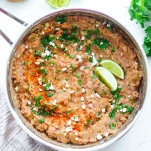 A sauce pan of refried beans with garnishing on top.