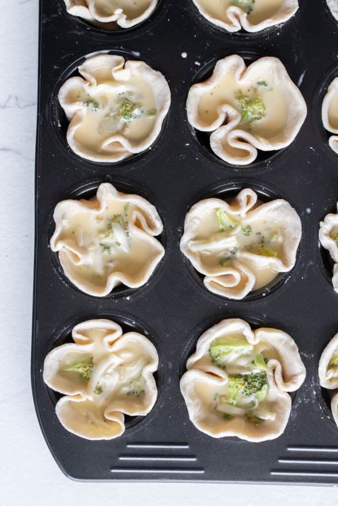 Cheese and egg mixture added to pie crusts in a muffin tin.