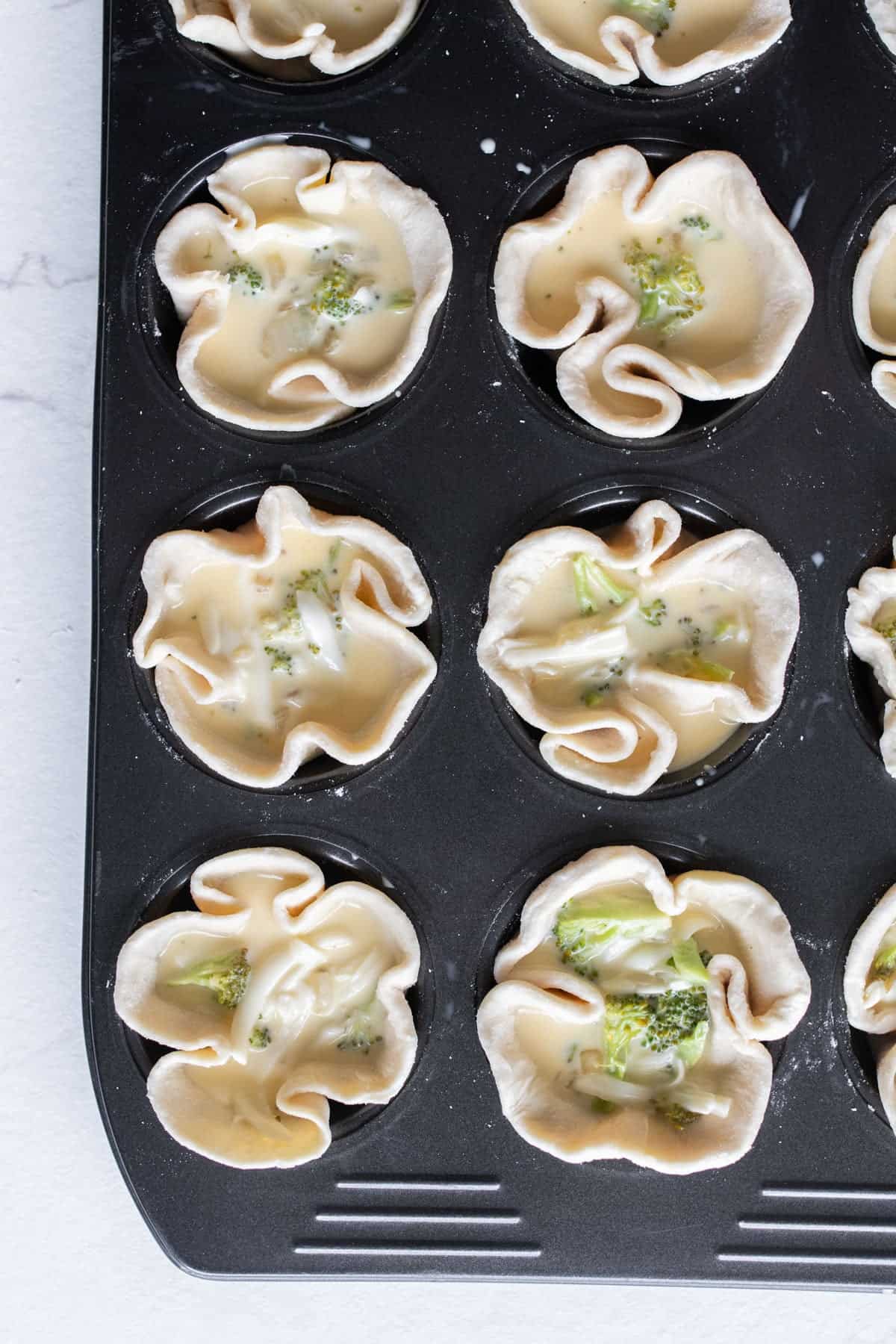 Cheese and egg mixture added to pie crusts in a muffin tin.