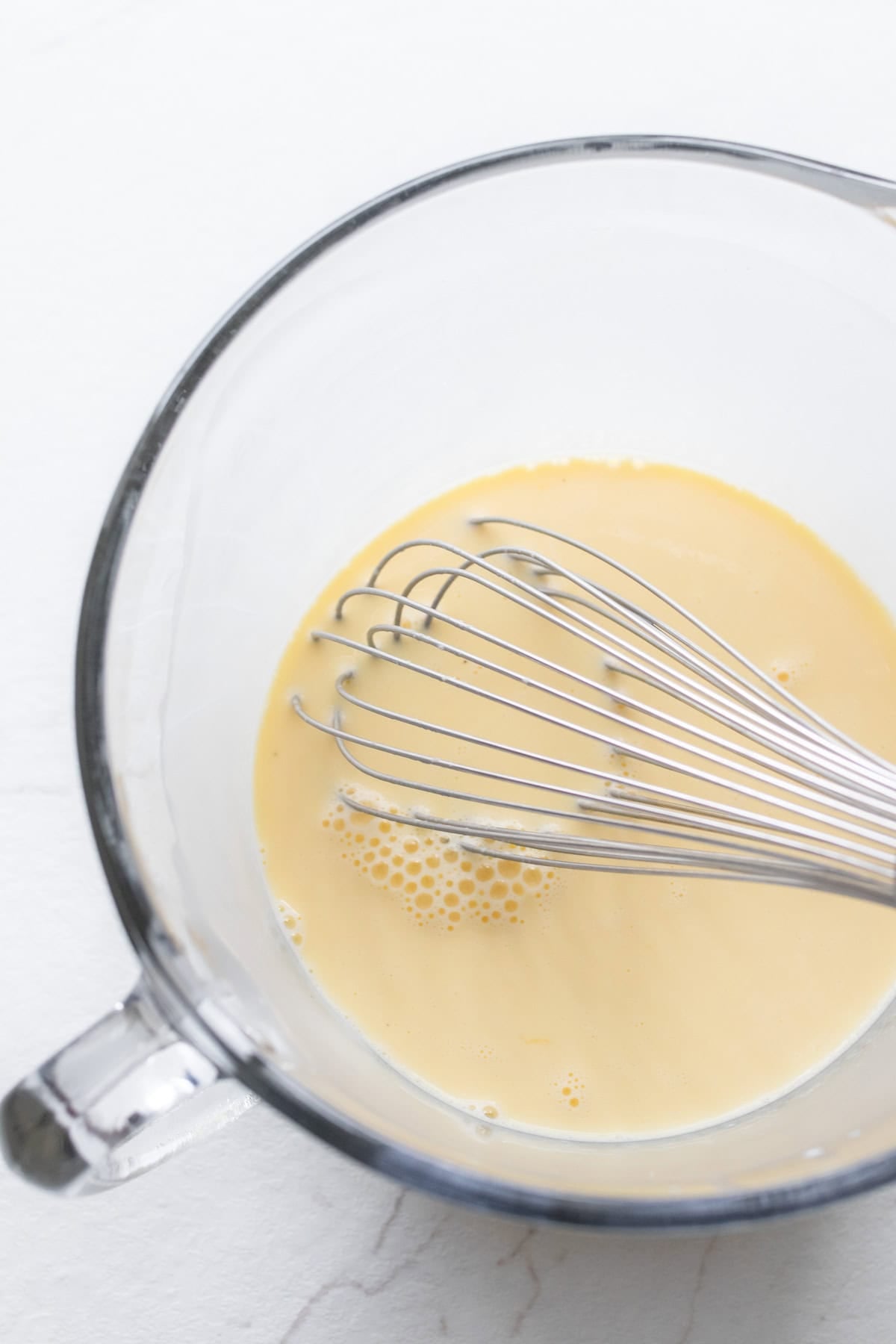 Eggs and cream mixed together in a glass measuring bowl with a whisk.