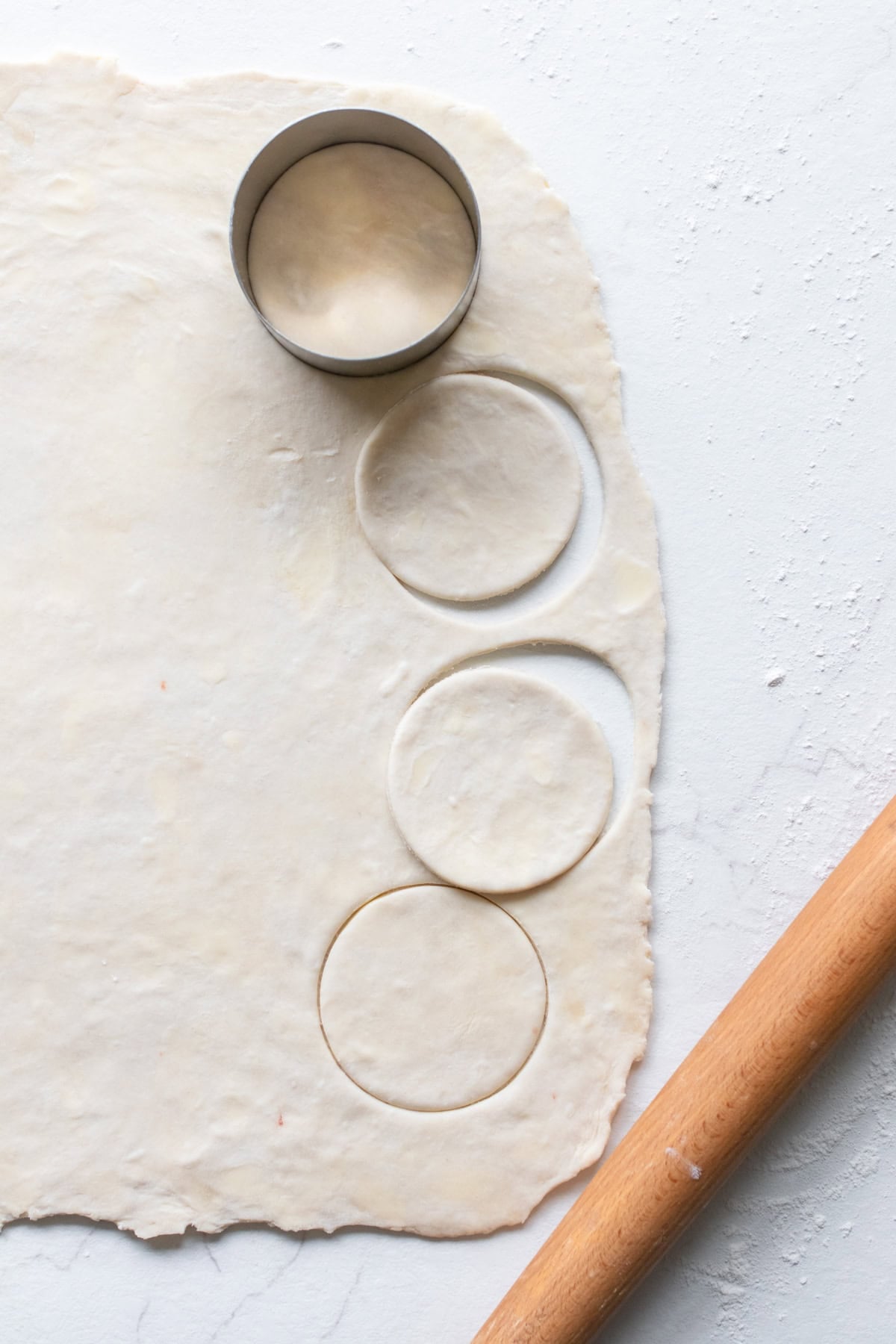 Dough rolled out on a counter top with a rolling pin and circles cut out of it.