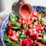 A large bowl of salad with a hand pouring pink salad dressing all over.