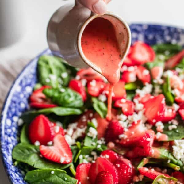 A large bowl of salad with a hand pouring pink salad dressing all over.