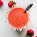 A bowl of strawberry salad dressing with a spoon in it and strawberries on the side on a counter top.