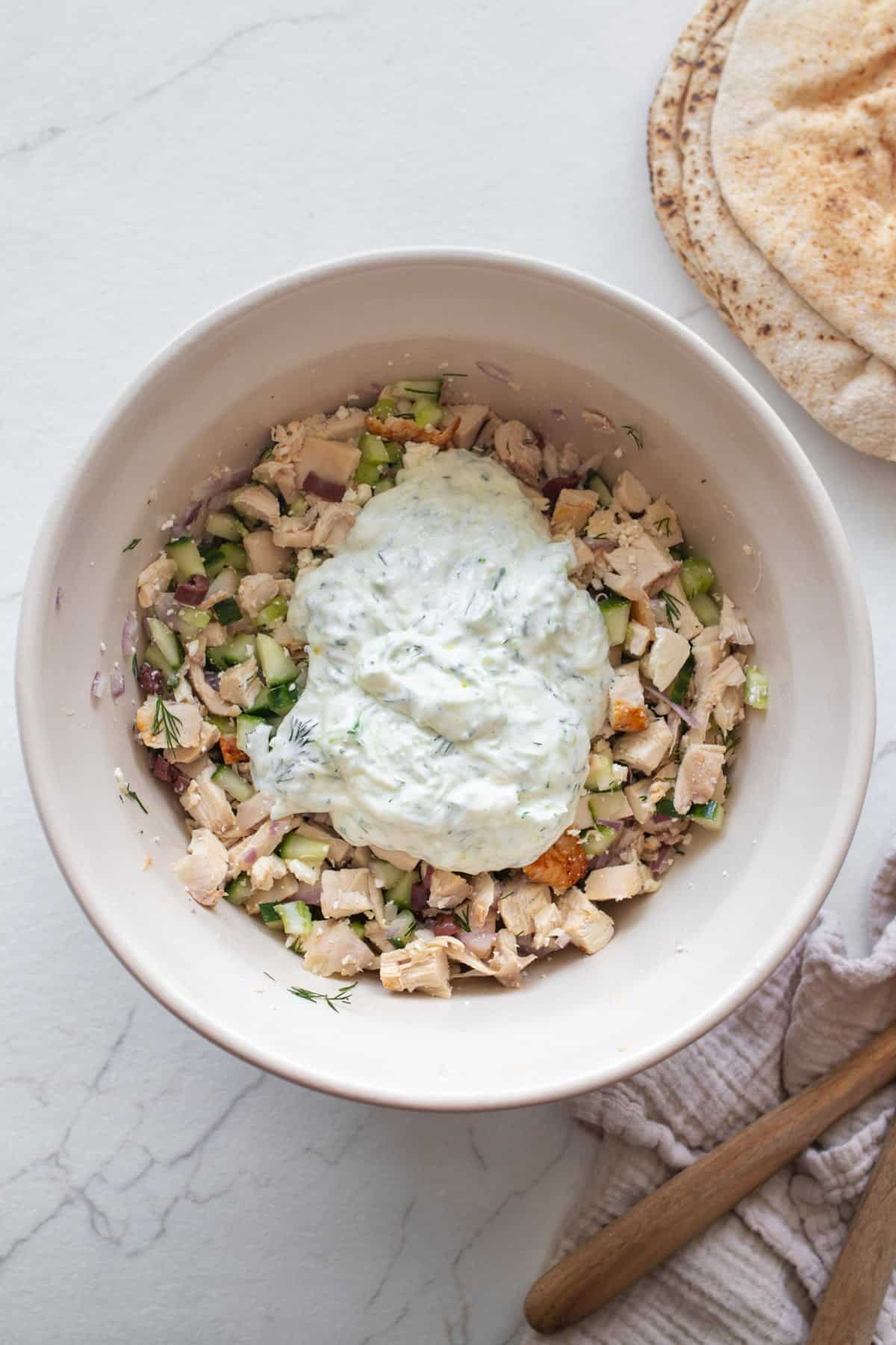 Tzatziki sauce on top of chopped chicken and veggies in a bowl.