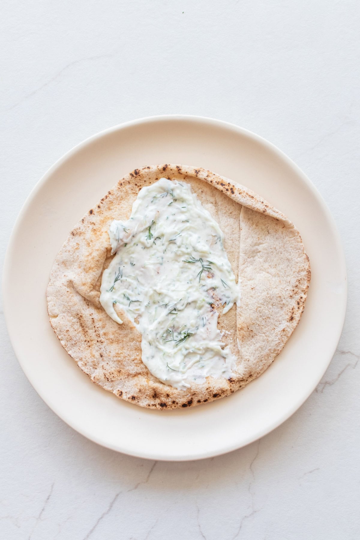 Tzatziki sauce on a pita on a plate.