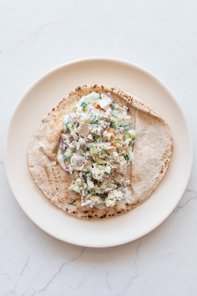 A plate with a pita topped with chicken salad.