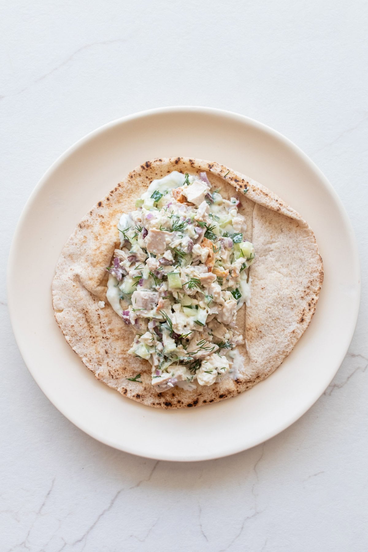 A plate with a pita topped with chicken salad.