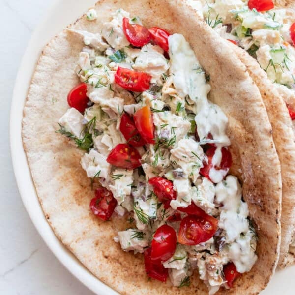 Pitas on a plate with tzatziki chicken salad in it and topped with tomatoes.