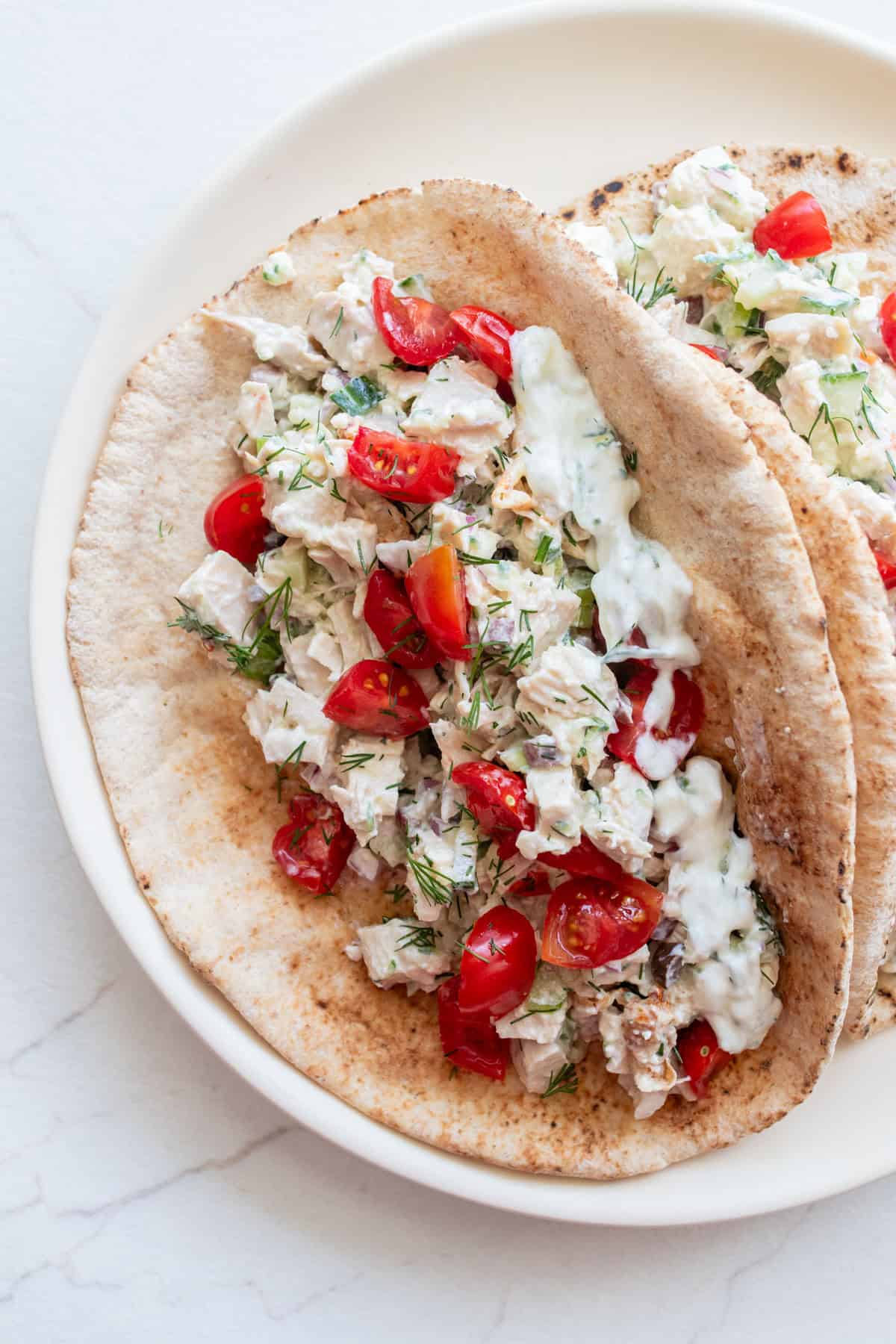 Pitas on a plate with tzatziki chicken salad in it and topped with tomatoes.