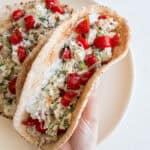 A hand picking up a pita filled with chicken salad off of a plate.