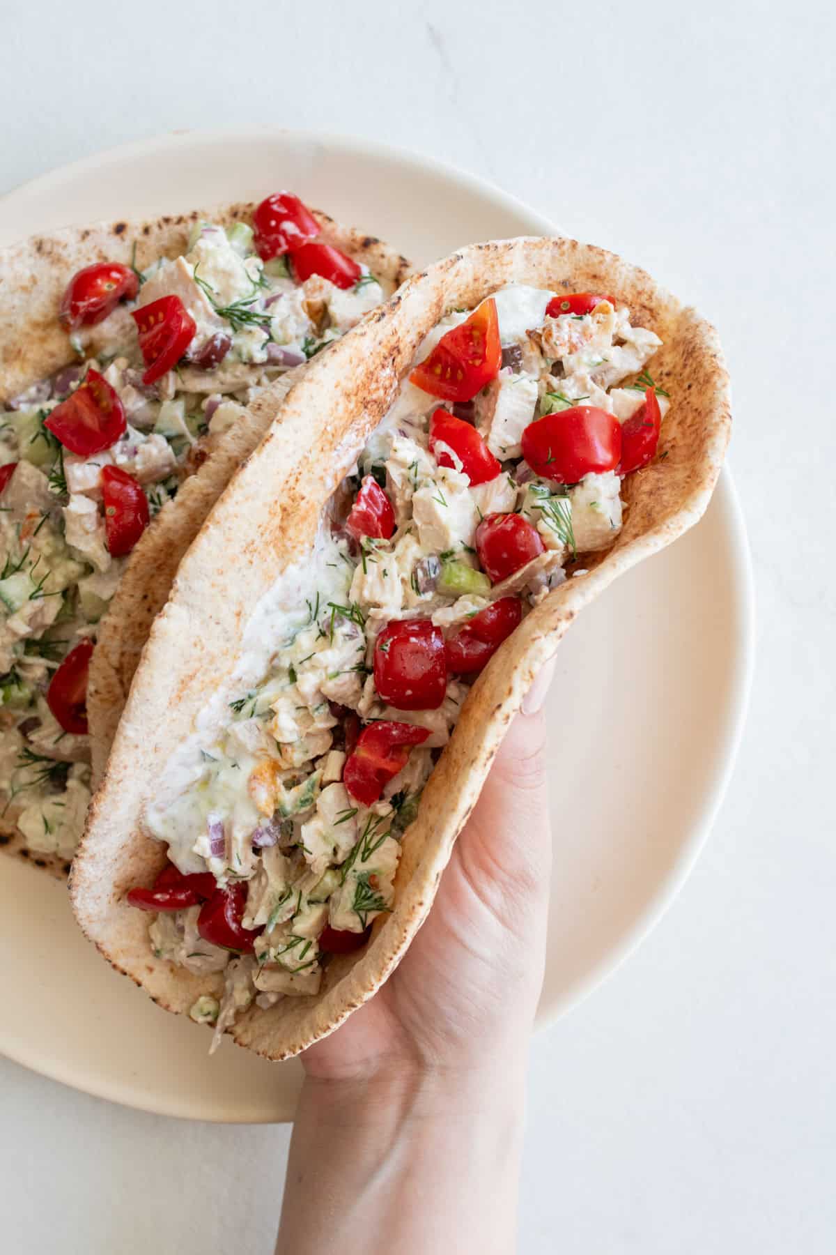A hand picking up a pita filled with chicken salad off of a plate.