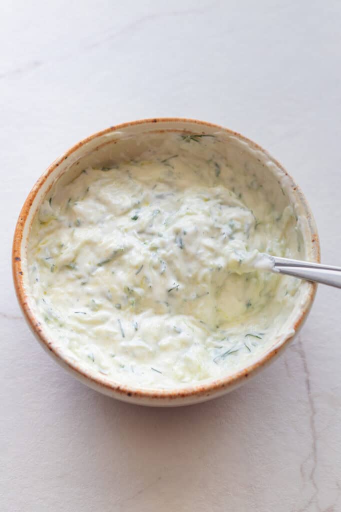 Tzatziki in a bowl with a spoon in it.