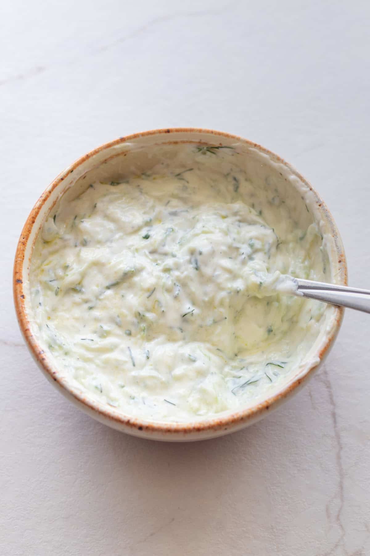 Tzatziki in a bowl with a spoon in it.