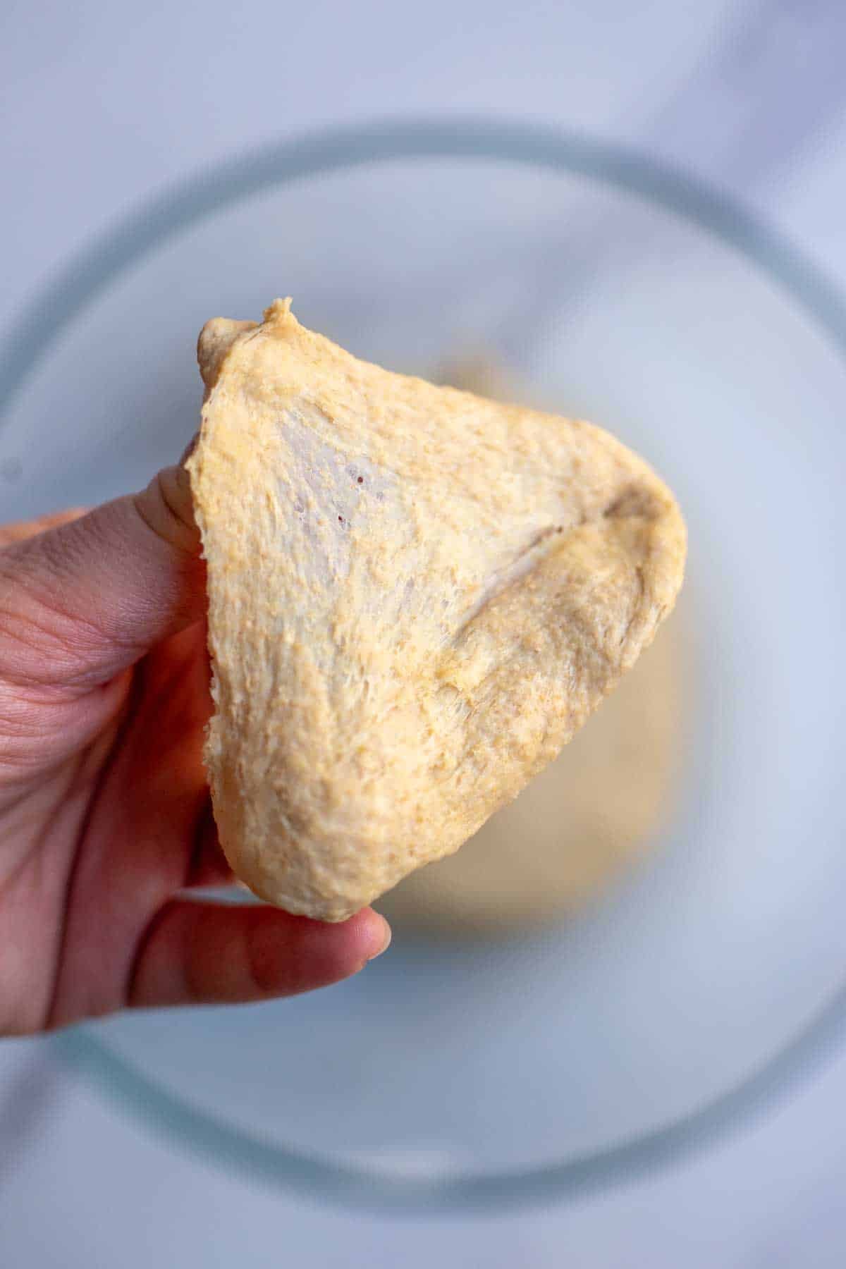 A hand holding a piece of dough demonstrating the window pane test.