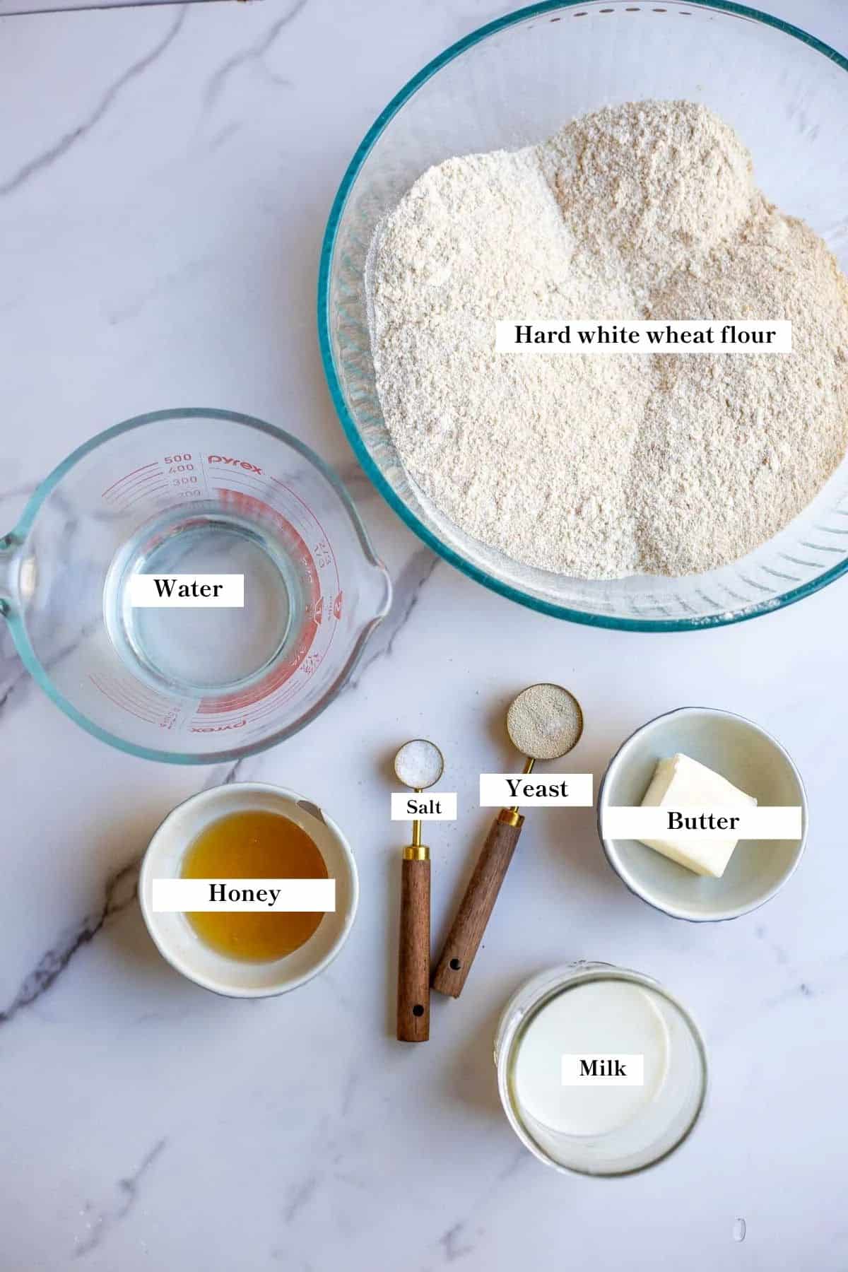 Ingredients for fresh milled sandwich bread in bowls on a white marble counter top.