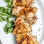 Four chicken thighs on a white platter with greens on the side.