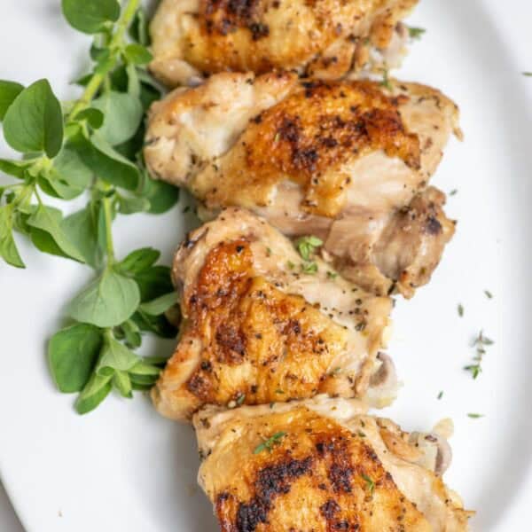 Four chicken thighs on a white platter with greens on the side.