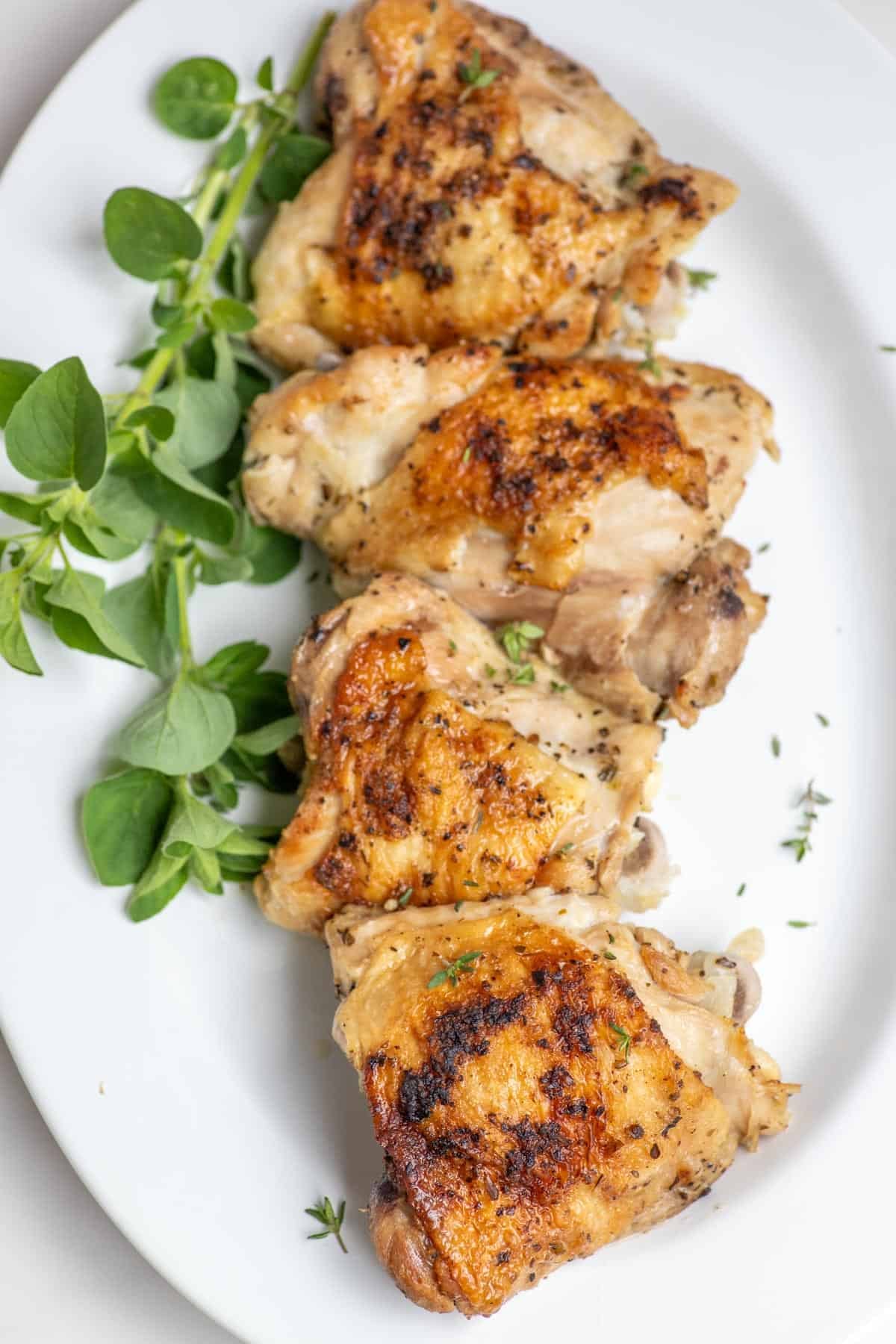 Four chicken thighs on a white platter with greens on the side.