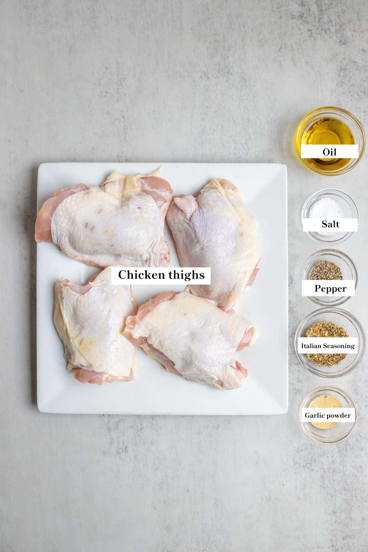 A white platter with four uncooked chicken thighs next to five clear glass bowls filled with seasonings and oil.