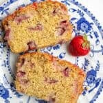 Two slices of strawberry bread on a blue and white plate with one strawberry on the side.