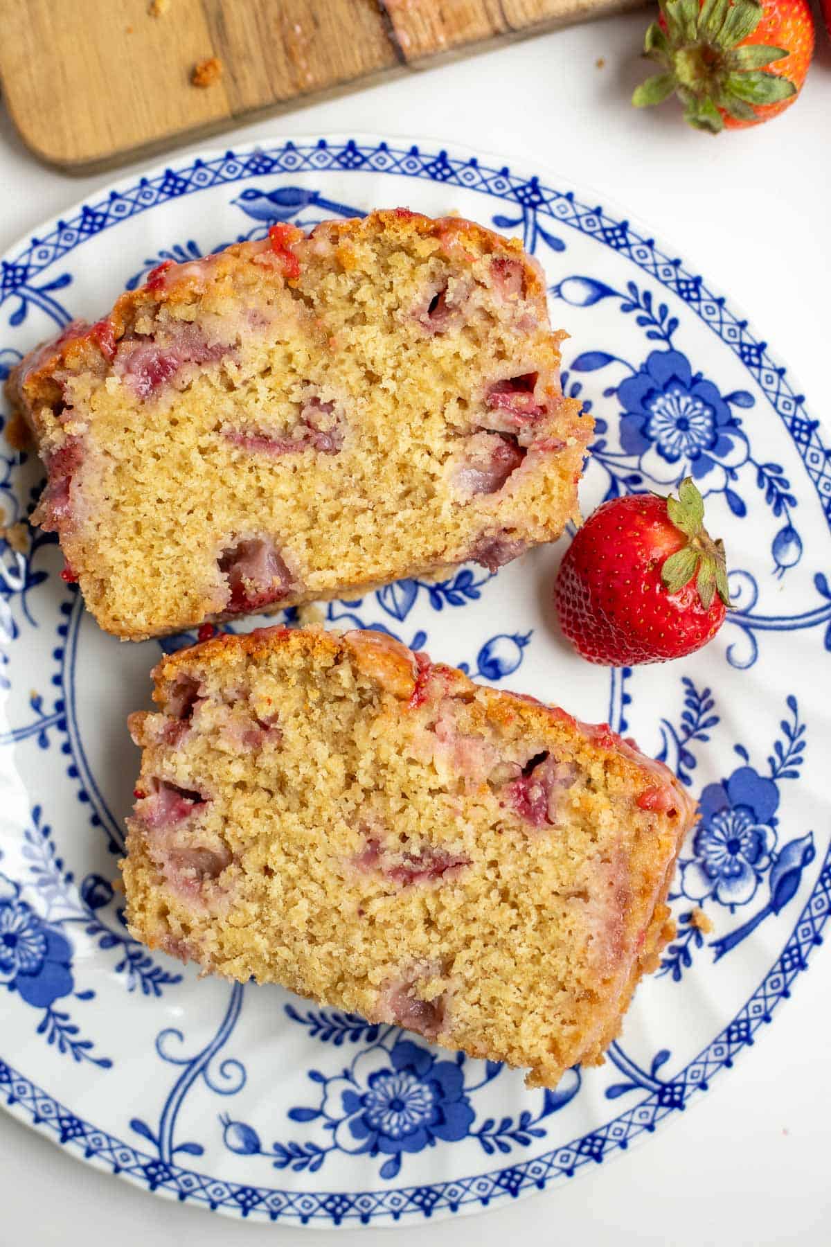 Two slices of strawberry bread on a blue and white plate with one strawberry on the side.