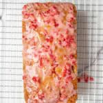 A loaf of strawberry bread with a strawberry glaze on top on a wire rack.