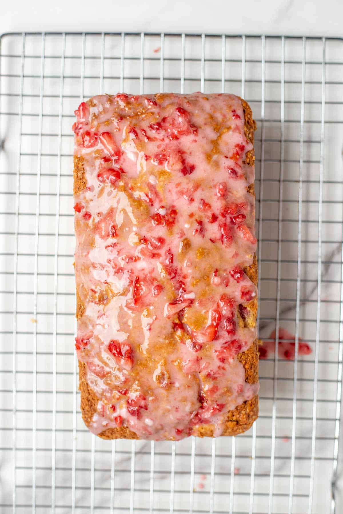 A loaf of strawberry bread with a strawberry glaze on top on a wire rack.