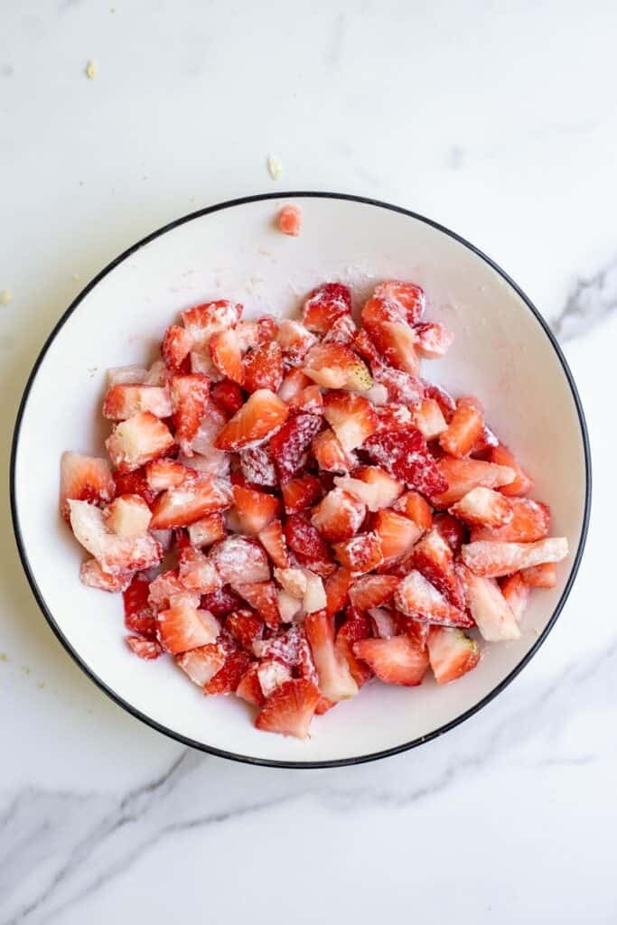 Chopped strawberries coated in flour in a white bowl.