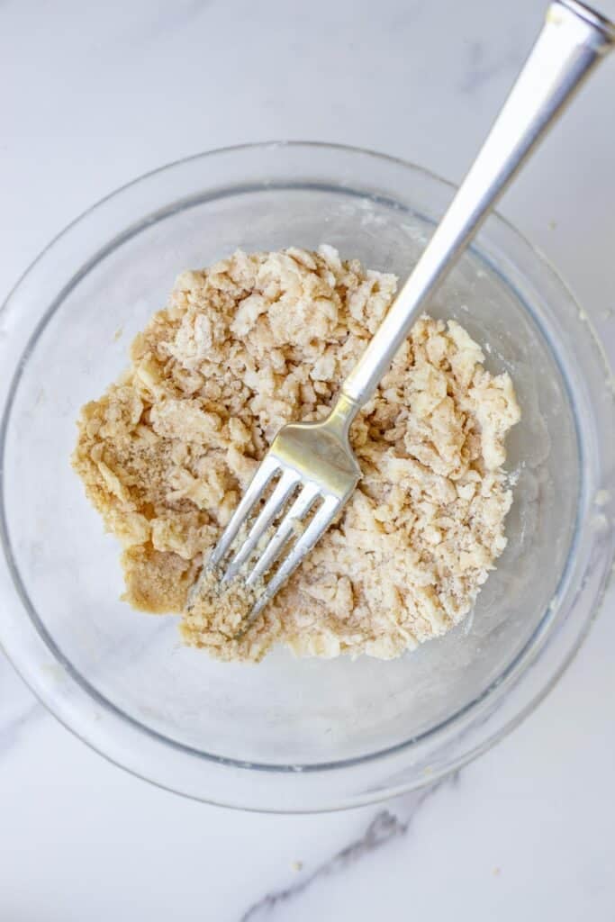 Flour, sugar, and cold butter crumbled together in a glass bowl.