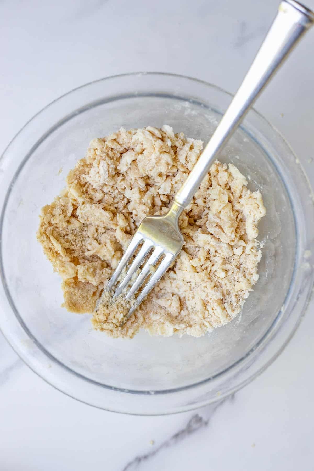 Flour, sugar, and cold butter crumbled together in a glass bowl.