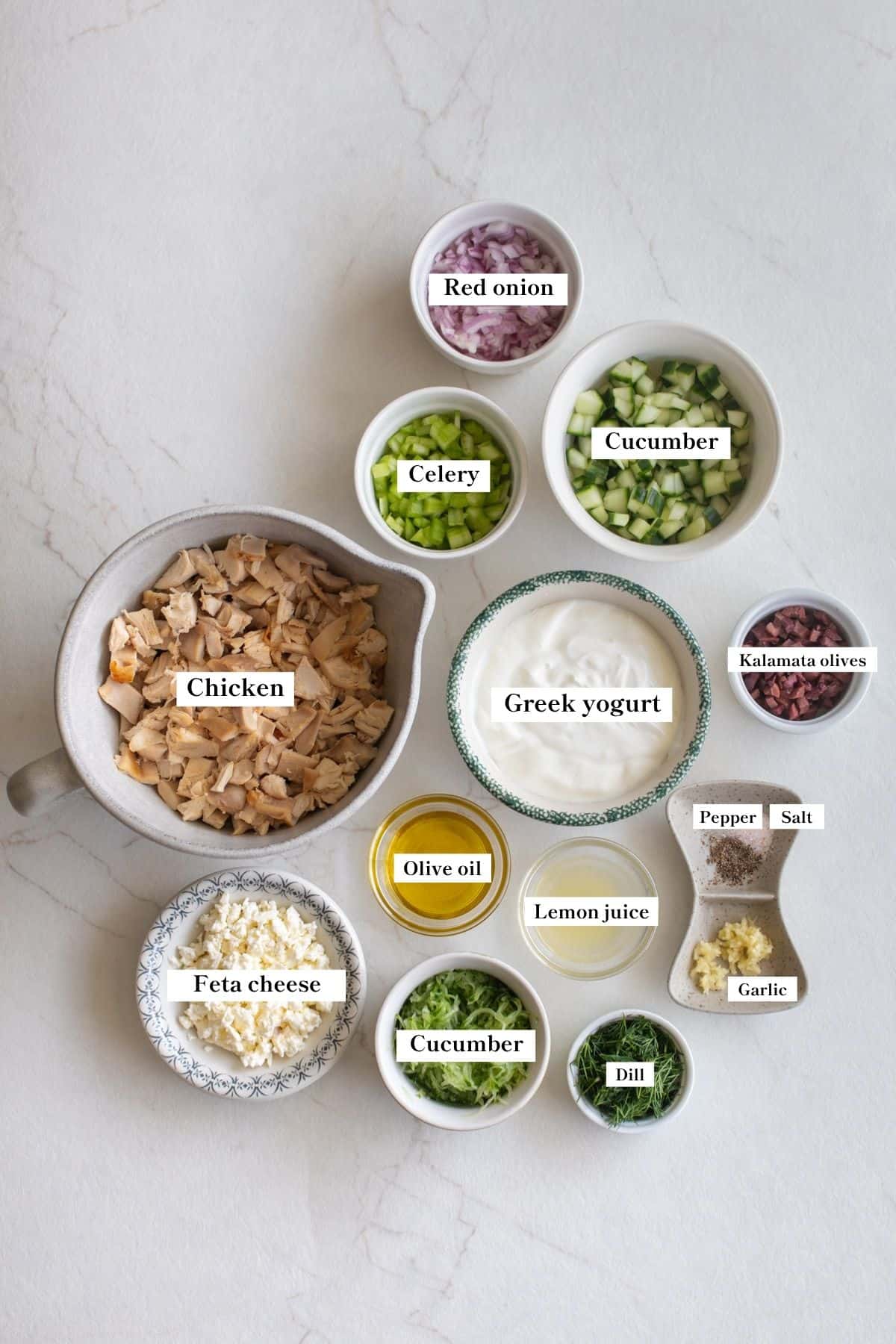 Ingredients for tzatziki chicken salad in bowls on a counter top.