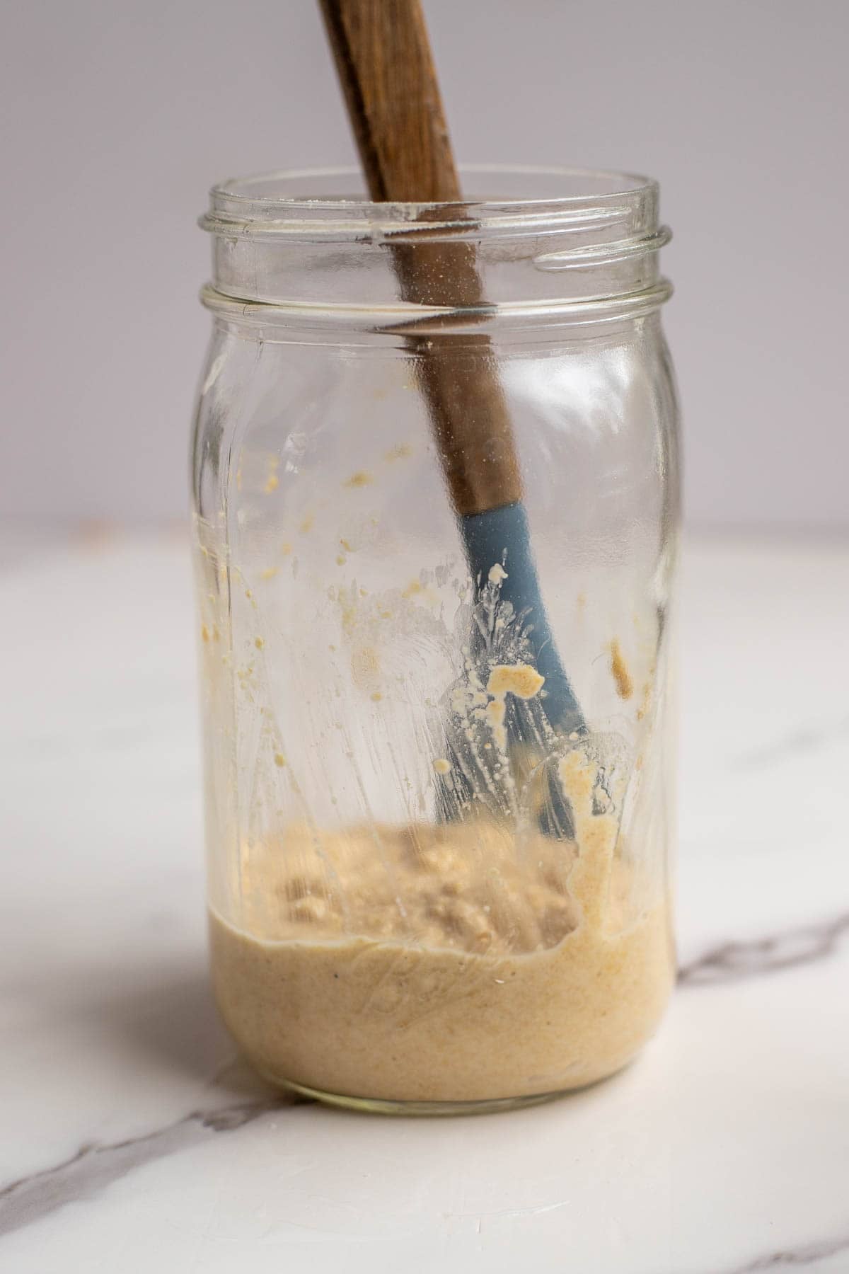 Using a silicone spatula to scrape down the sourdough starter from the sides of a mason jar.