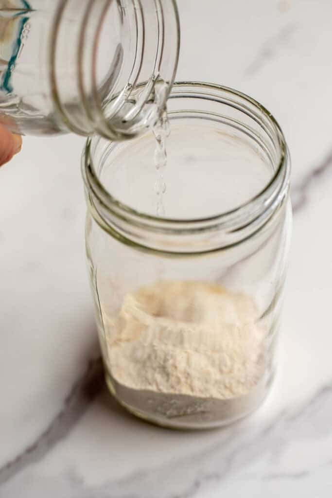Adding water to a glass jar with flour.