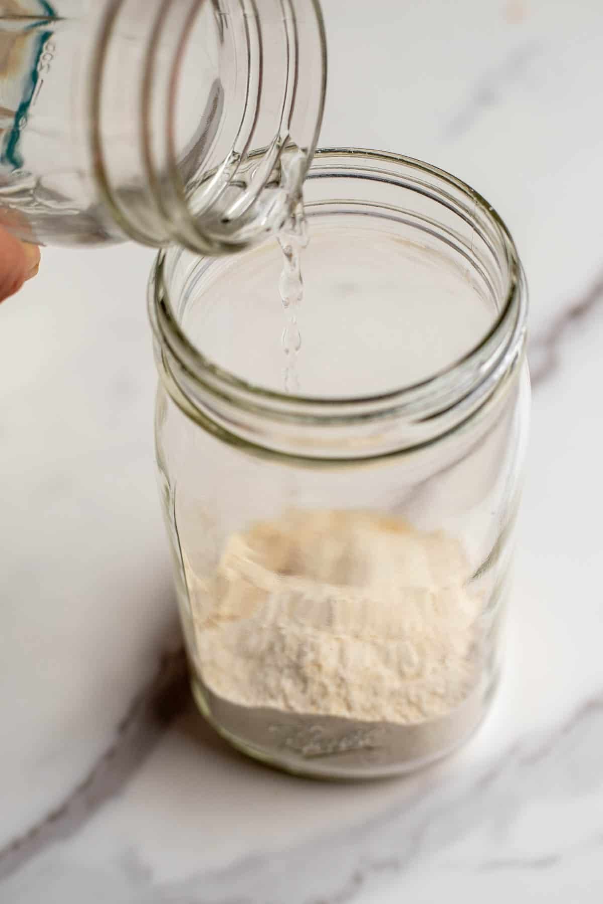 Adding water to a glass jar with flour.