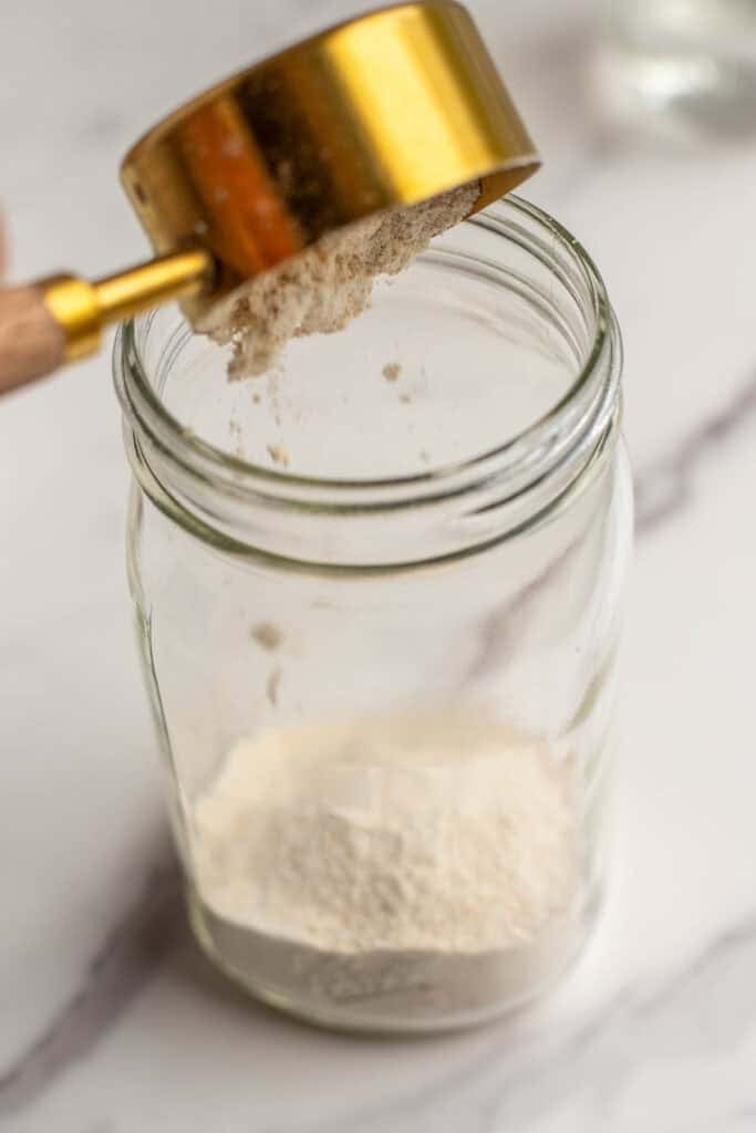 A measuring cup pouring flour into a glass mason jar.