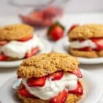 Three plates of whole wheat strawberry short cake with whipped cream and whole strawberries.