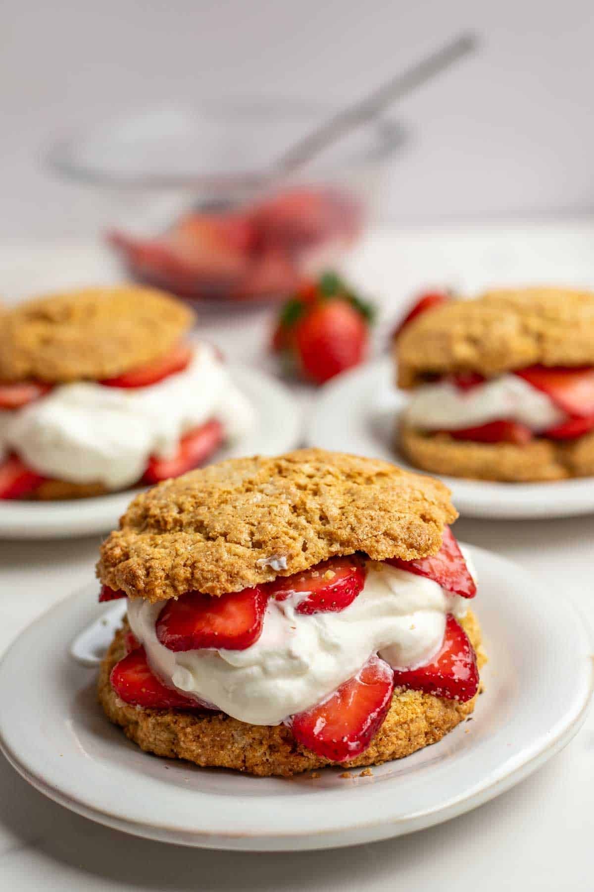Three plates of whole wheat strawberry short cake with whipped cream and whole strawberries.