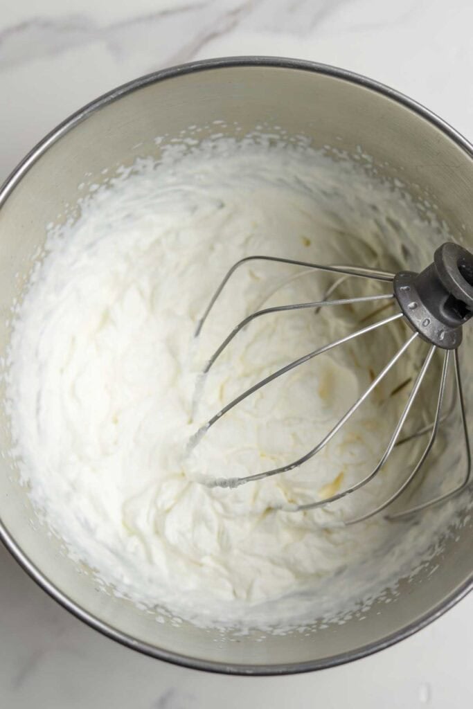 Whipped cream in the stand mixer bowl with a whisk attachment.