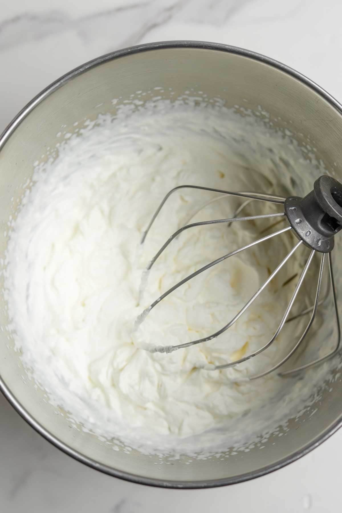 Whipped cream in the stand mixer bowl with a whisk attachment.
