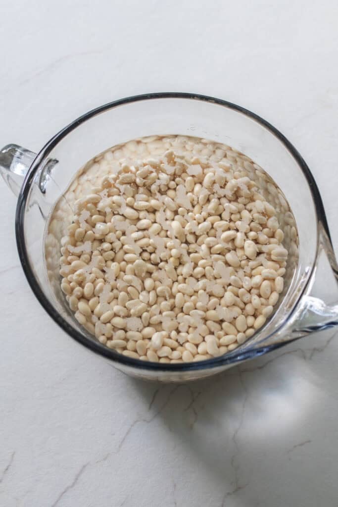 Beans soaking in water in a glass measuring bowl.