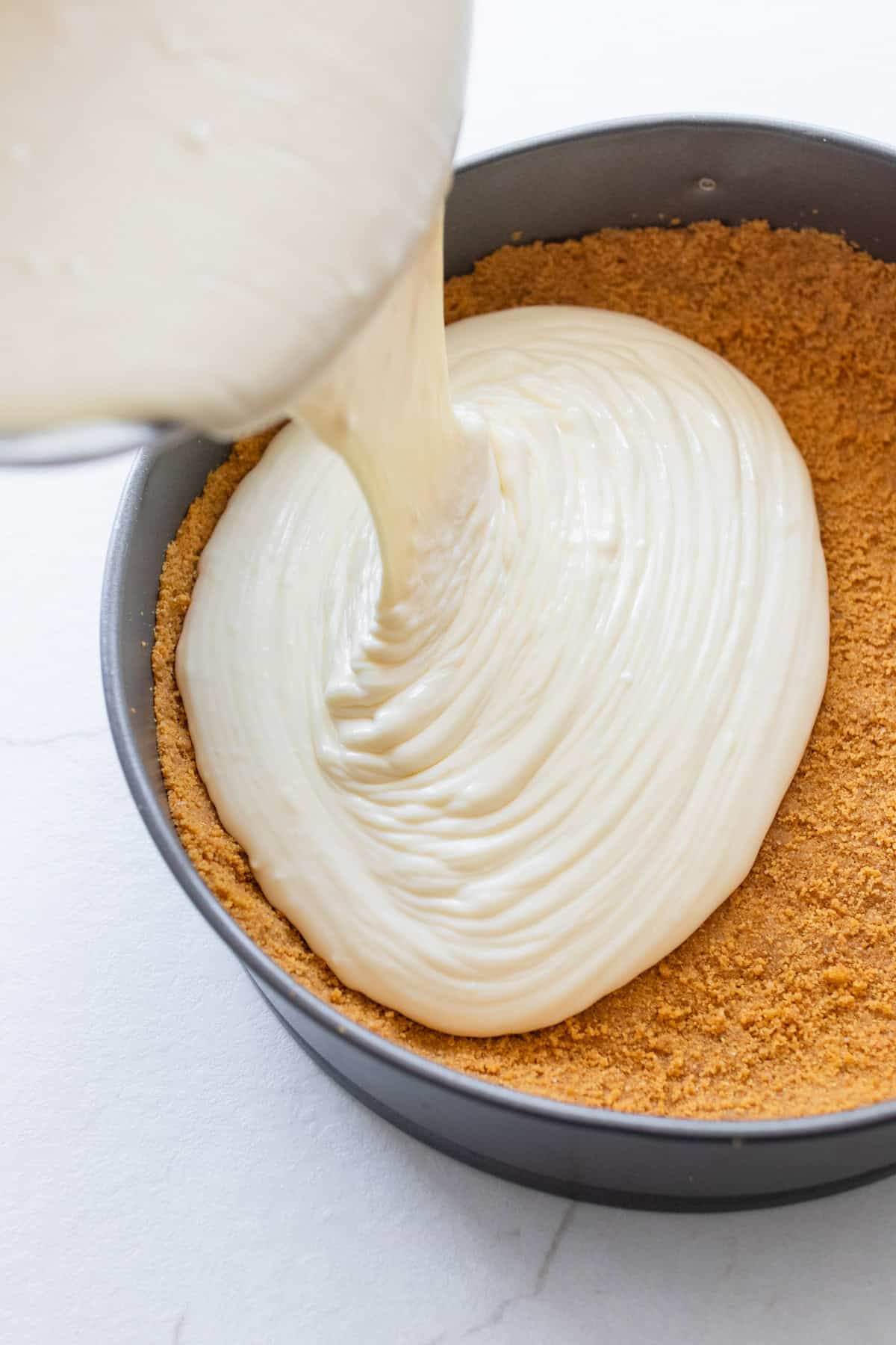 Cheesecake batter poured into a springform pan that has a graham cracker crust.