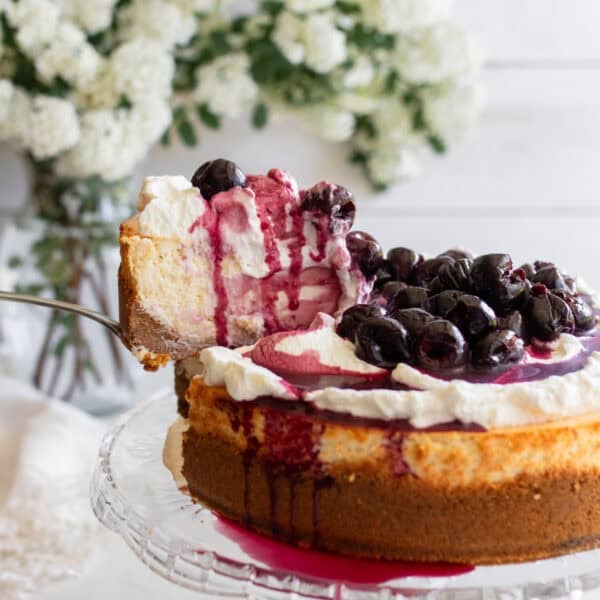 a slice of cheesecake lifted out of a whole cheesecake on a cake platter.