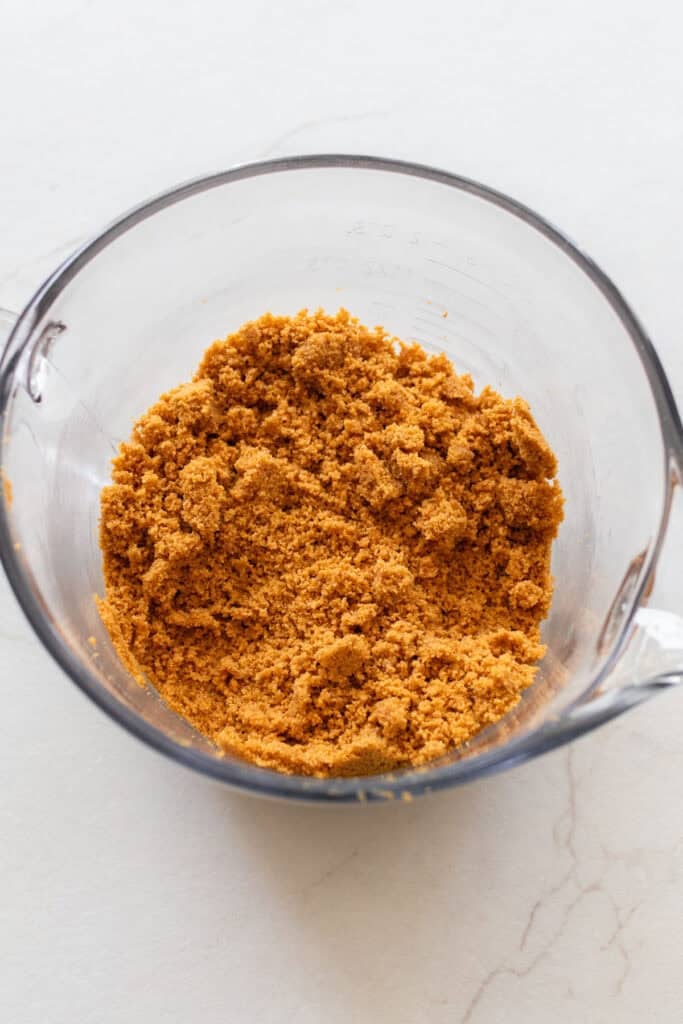Graham cracker crumbs mixed with butter in a glass measuring bowl.